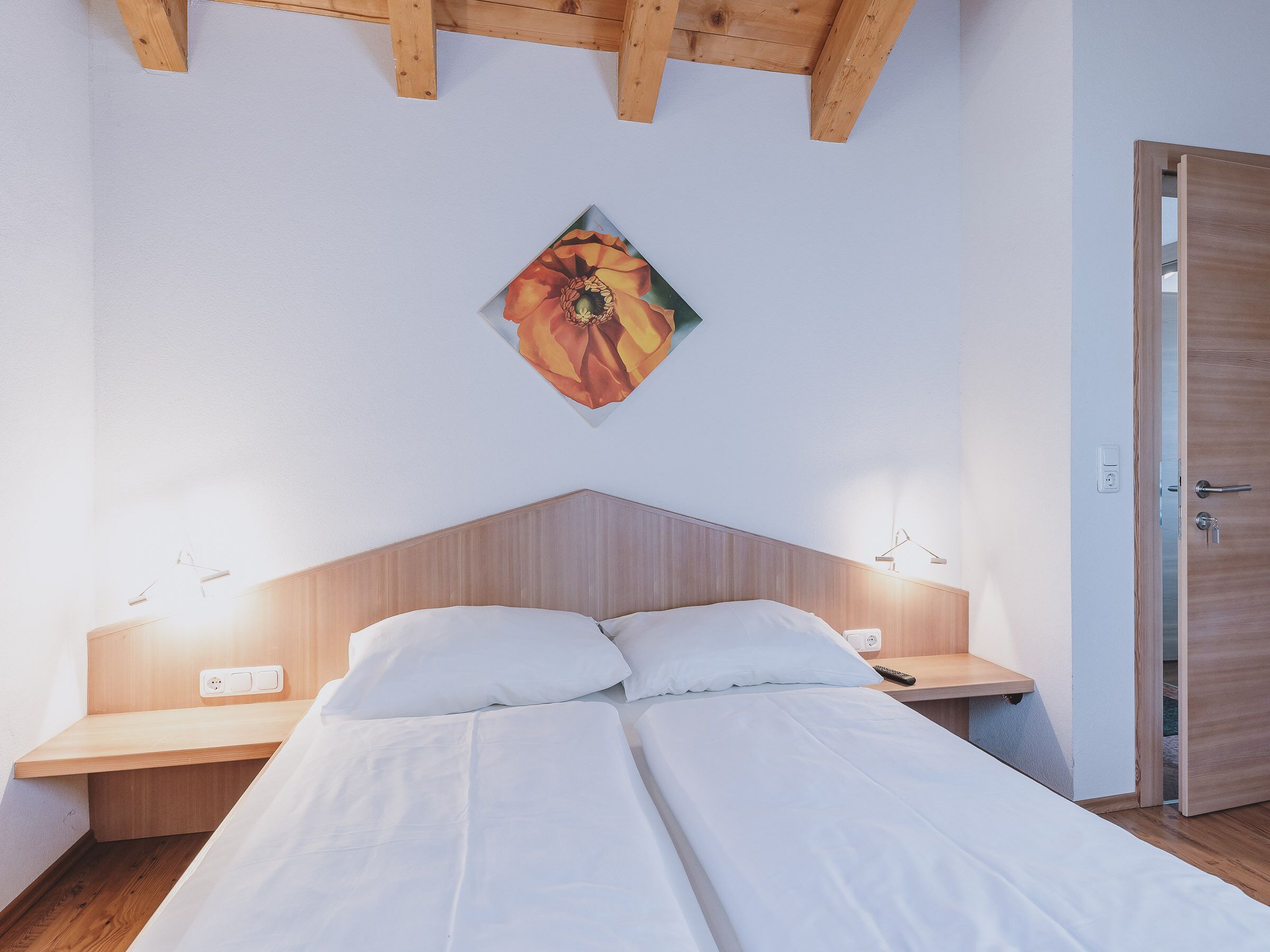 Une chambre avec un lit, des tables de chevet, une tête de lit en bois, un tableau et une porte.