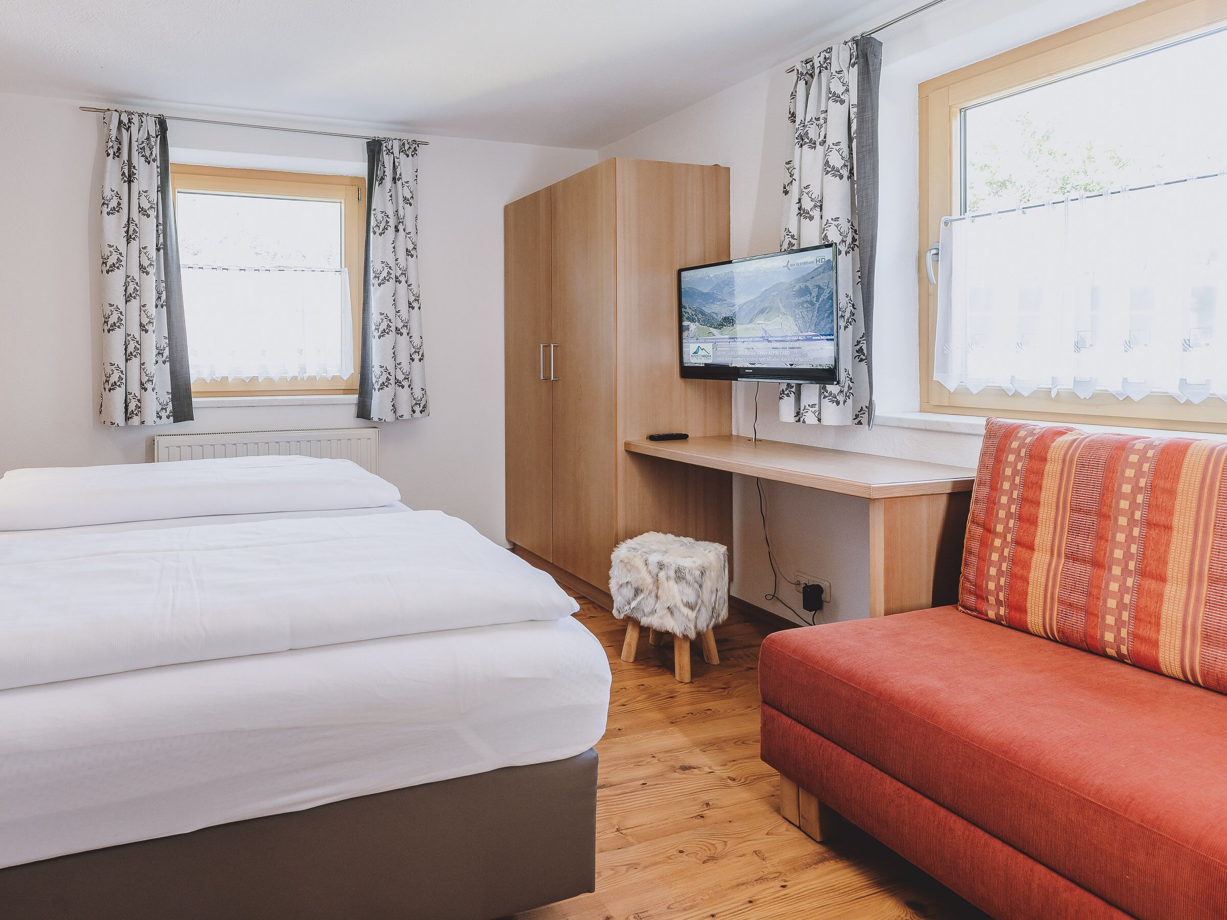 A bedroom with a bed, a desk, a television, and a sofa.