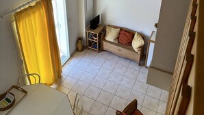 Ein gemütlicher Wohnraum mit Holzboden, einem weißen Sofa, einem kleinen Tisch und einem Fenster mit gelben Vorhängen.