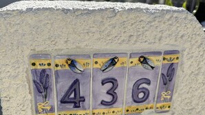Eine an der Wand befestigte Nummernschild mit der Nummer 436, verziert mit Vögeln und Blumen.