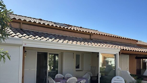Eine überdachte Terrasse mit Tisch und Stühlen, eine Glasschiebetür und ein Ziegeldach.
