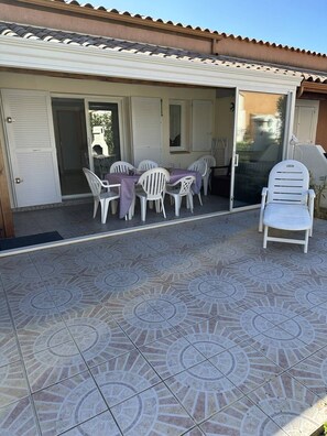 Relax on the covered patio with a table and chairs, surrounded by a building with a sliding glass door.