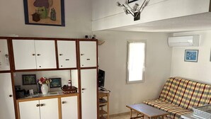 Eine kleine Küche mit Esstisch, der mit einer Schokoladen-Tischdecke bedeckt ist, einer Couch und einem kleinen Fernseher.