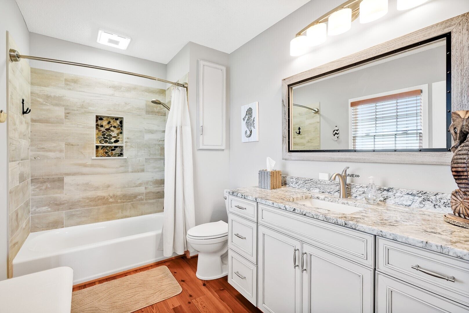 A modern bathroom with a bathtub, toilet, and vanity with a large mirror.