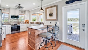 A kitchen with white cabinets, a central island, and a view of the outdoors. - Spacious 5BR, 4BA home at Holden Beach with stunning water views. (Holden Beach)