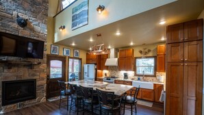 A spacious kitchen with a large island, wooden cabinets, and a stone fireplace. - 22 Acre retreat, Pet Friendly, View, Privacy (Eureka Springs)