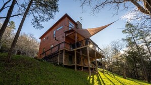 A modern wooden house with a unique sloped roof, situated on a grassy hill surrounded by trees. - 22 Acre retreat, Pet Friendly, View, Privacy (Eureka Springs)