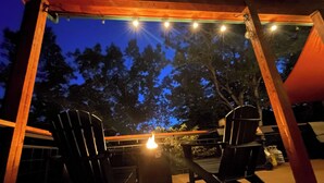 An outdoor patio with two Adirondack chairs, a table, and string lights. - 22 Acre retreat, Pet Friendly, View, Privacy (Eureka Springs)