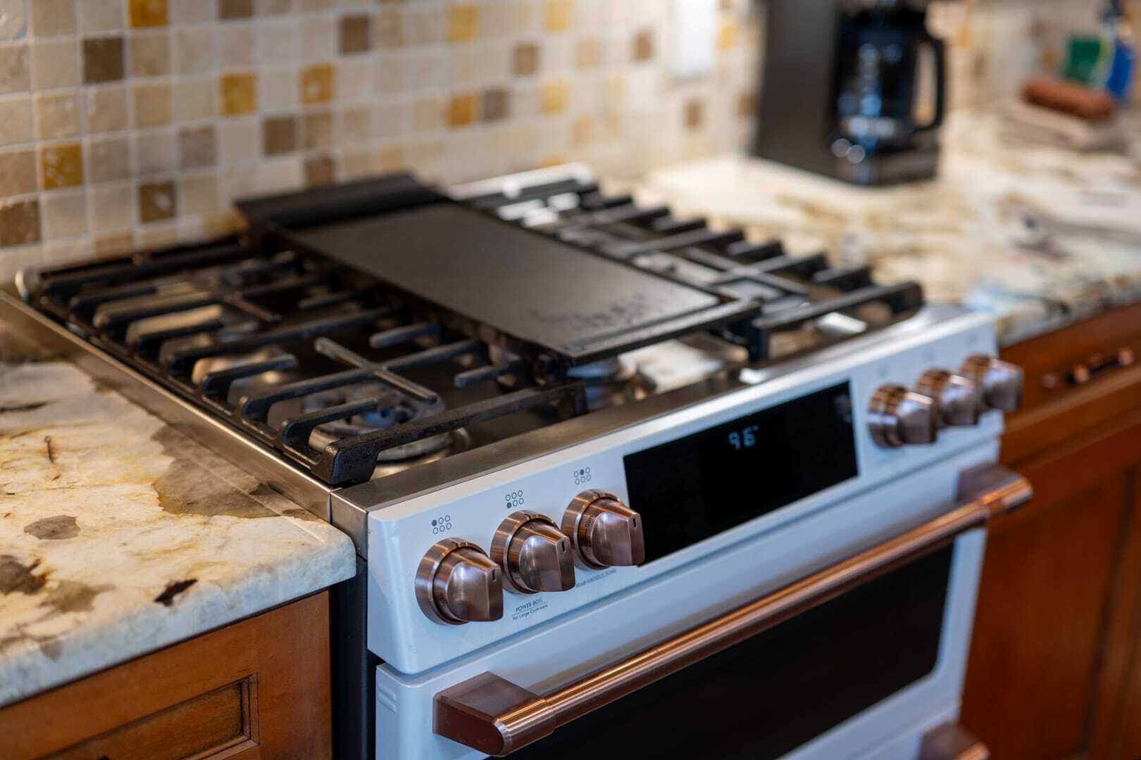 Een keuken met een gasfornuis, oven en een digitaal scherm.