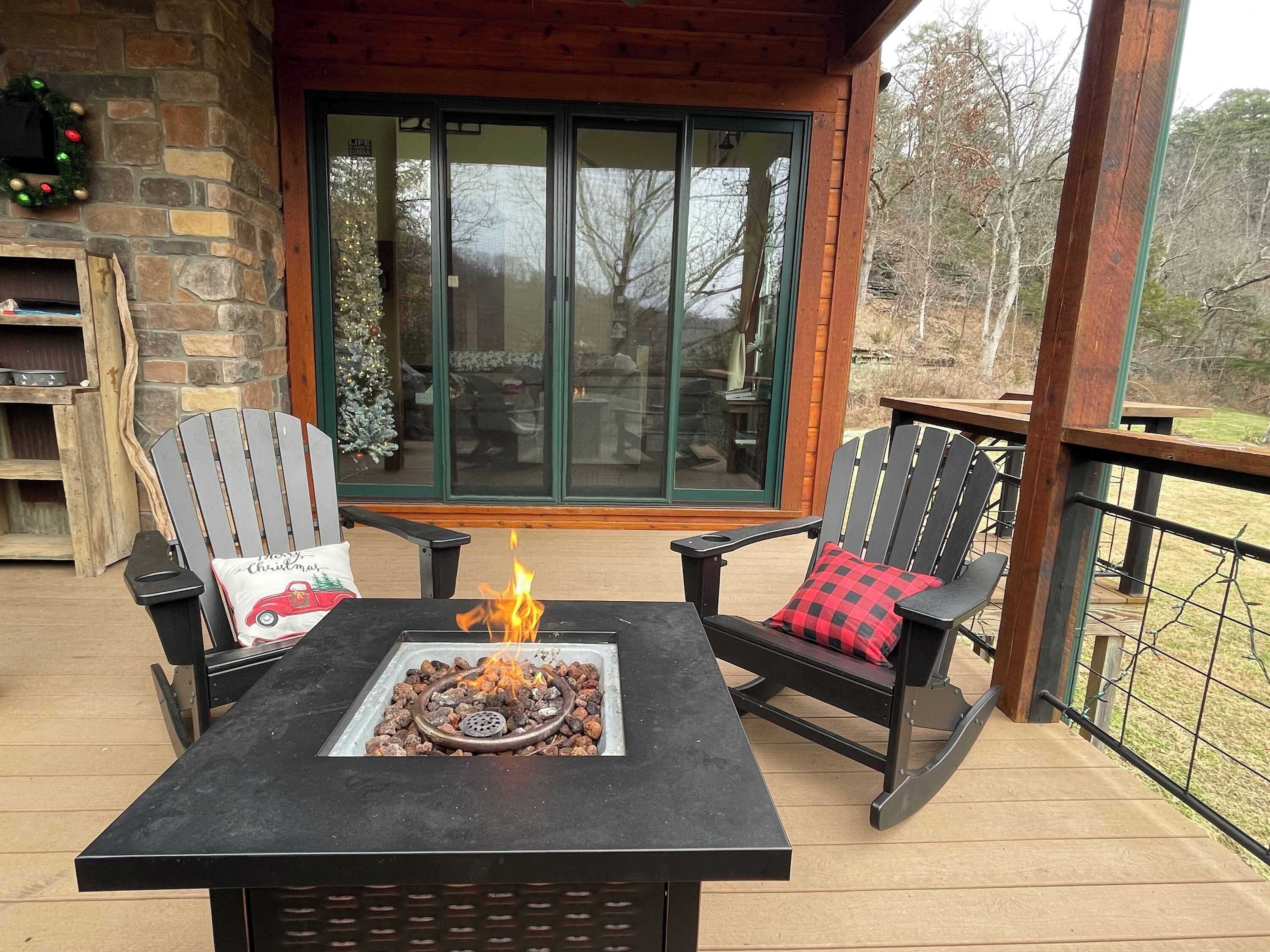 Una terraza con dos sillas Adirondack, una mesa cuadrada y un pozo de fuego, además de un muro de piedra.