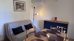 Une pièce chaleureuse avec un canapé à rayures, une table à manger en bois surmontée de sets de table en fibres tressées, un buffet bleu contenant de la vaisselle et un climatiseur fixé au mur.