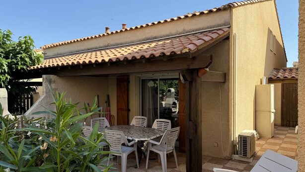 Eine Terrasse mit Tisch und Stühlen, ein kleiner überdachter Bereich und ein Kühlschrank.