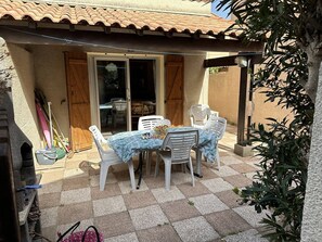 Een terras met een tafel, stoelen, een schuifpui en een betegeld dak.