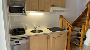 Eine kompakte Küche mit Holzausstattung, einer Edelstahl-Spüle, einer Mikrowelle, einem Einbauofen und einem Geschirrspüler.