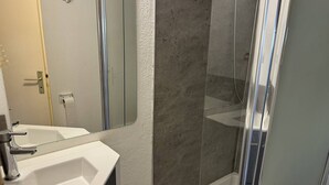 Ein Badezimmer mit Waschbecken, Spiegel, Duschkabine und Handtuchhalter.