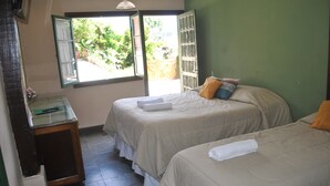 Una habitación con dos camas, un escritorio pequeño y una ventana con una persiana abierta.