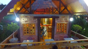 Maqueta de un edificio rústico con techo de madera, una puerta central y un comedor con mesas y sillas.