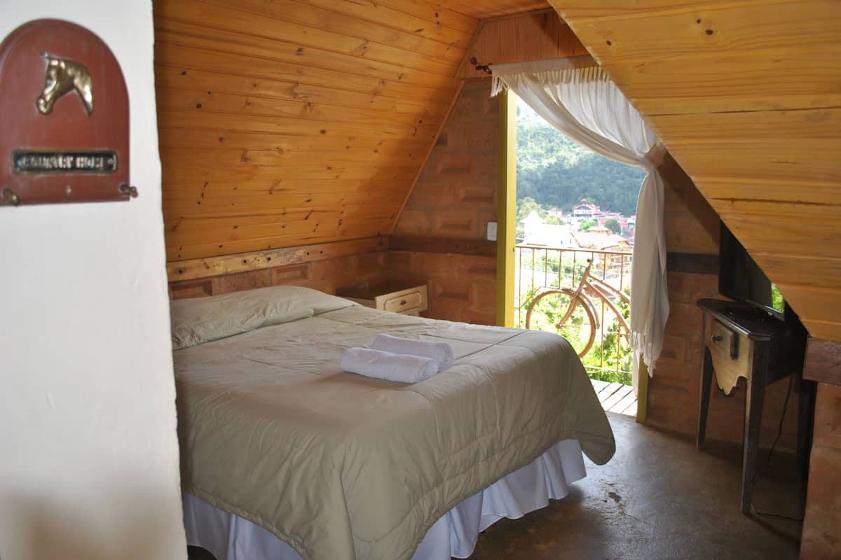 Una habitación acogedora con techo de madera, una cama con colcha blanca, una mesita y vistas a un balcón con una bicicleta.