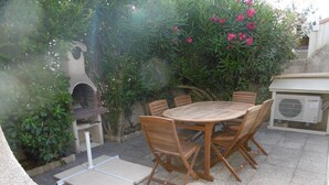 Eine Terrasse mit einem runden Holztisch und Stühlen, umgeben von Pflanzen und einem Grill.