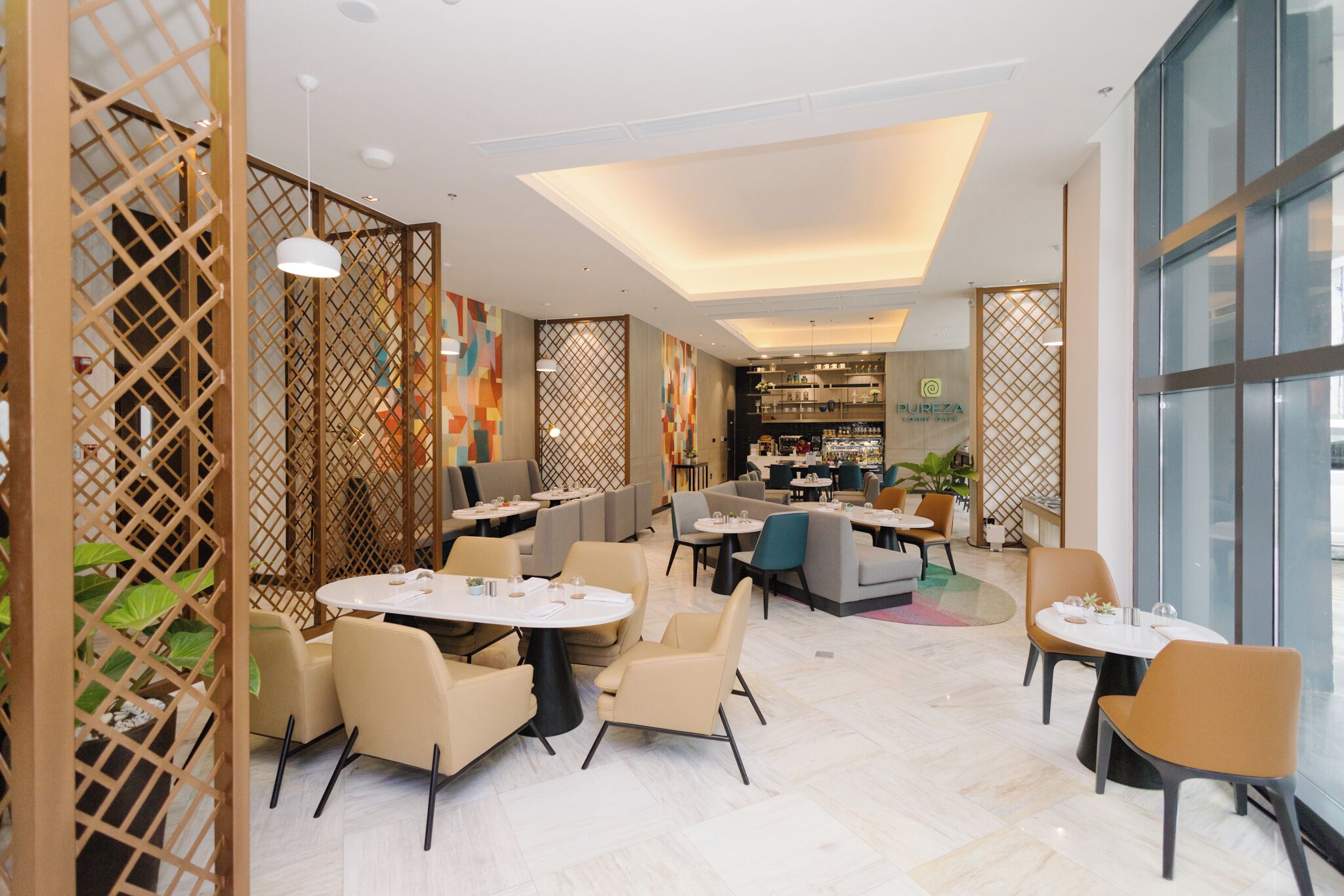 A modern restaurant with round tables and chairs, a visible bar area, and a decorative partition with plants.