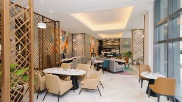 A modern restaurant with round tables and chairs, a visible bar area, and a decorative partition with plants.