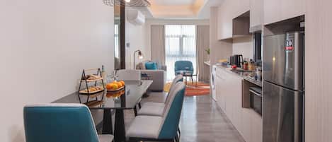 A modern kitchen with a stainless steel refrigerator, a dining area with a table and chairs, and a ceiling light fixture.