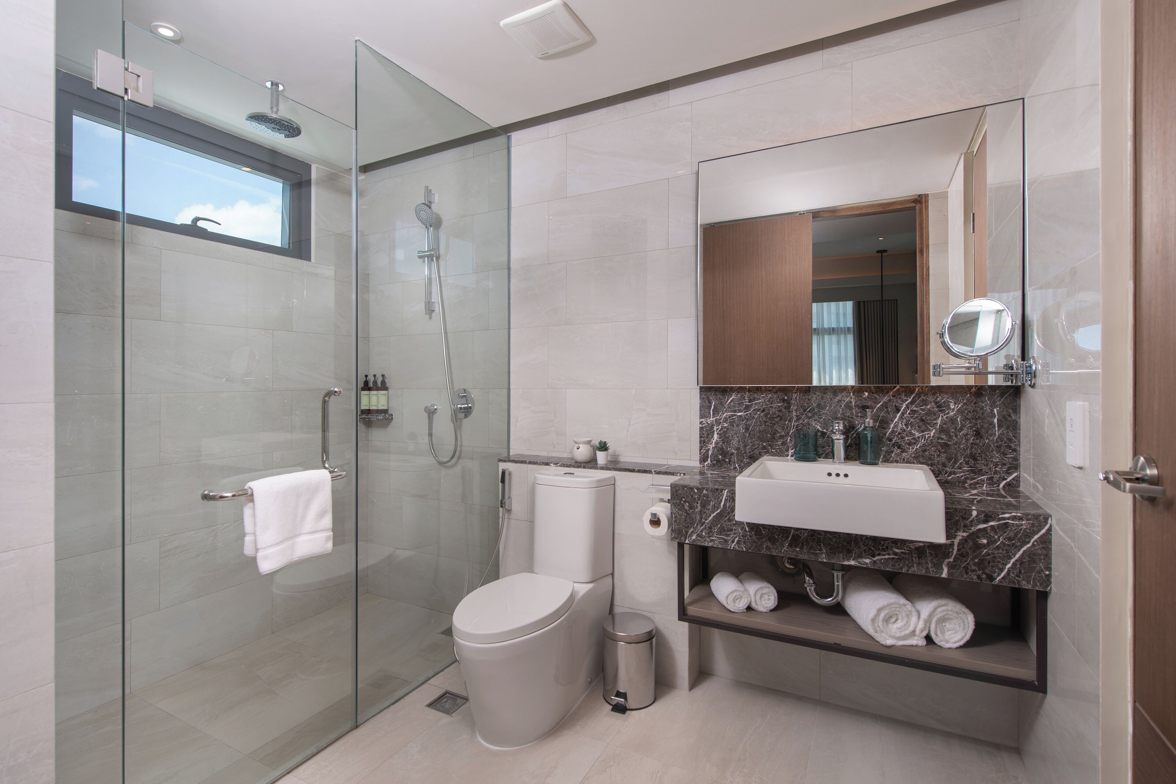 A modern bathroom with a glass-enclosed shower, a toilet, a sink with a marble countertop, and a mirror.