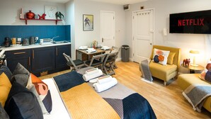 A modern hotel room with a bed, two sofas, a dining area, and a TV displaying 'NETFLIX'.
