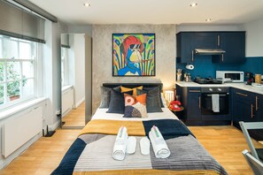 Een moderne slaapkamer met een groot bed, uitzicht op de keuken, en een kleurrijk schilderij aan de muur.
