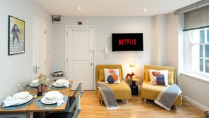 A modern hotel room with two beds, a dining area, and a TV displaying 'NETFLIX'.