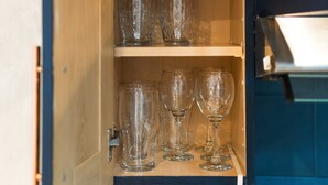 A kitchen cabinet with shelves holding glass jars and wine glasses.