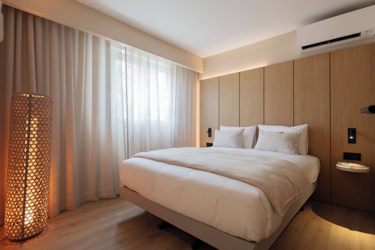 A modern bedroom with a large bed, a bedside table, a wall-mounted air conditioner, and a floor lamp.