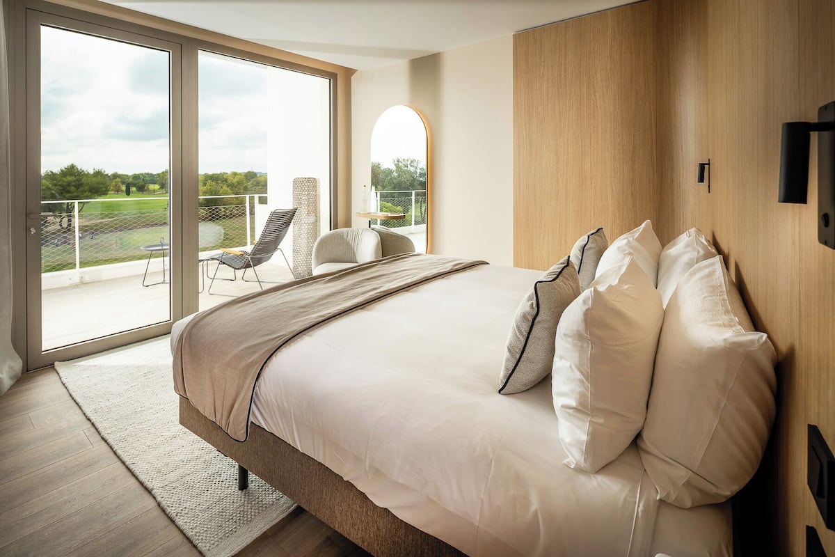 A bedroom with a large bed, a TV, and a balcony with a chair.