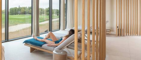 Une salle de spa dotée de grandes fenêtres, d’une table de massage et d’une cloison en bois.
