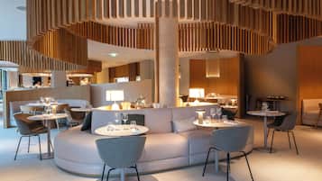 A modern restaurant with round tables, cushioned seating, and wooden paneling.