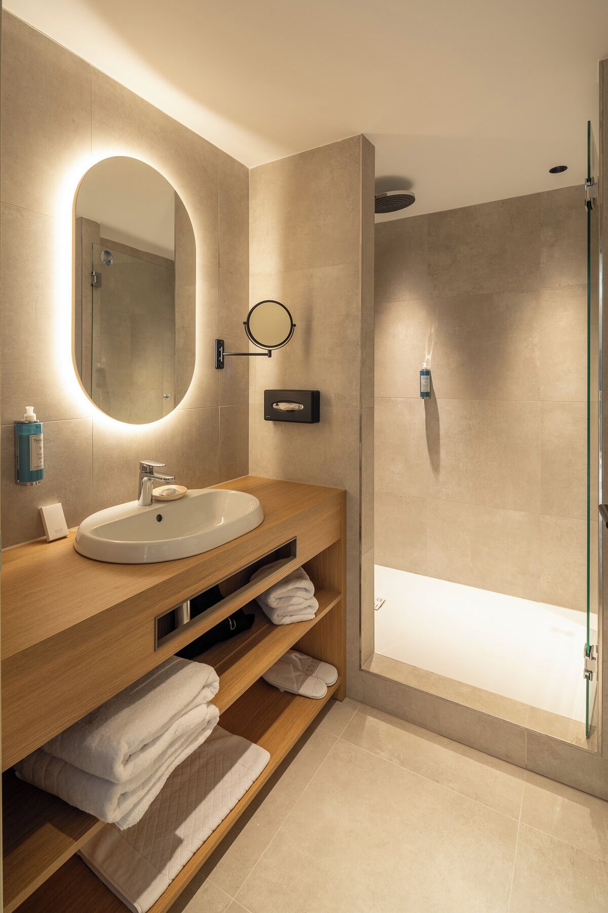 A modern bathroom with a round mirror, a sink, and a glass-enclosed shower.