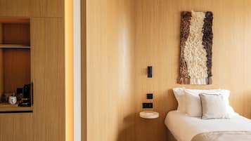 A modern hotel room with a wooden wardrobe, a bed with white bedding, and a textured wall hanging.