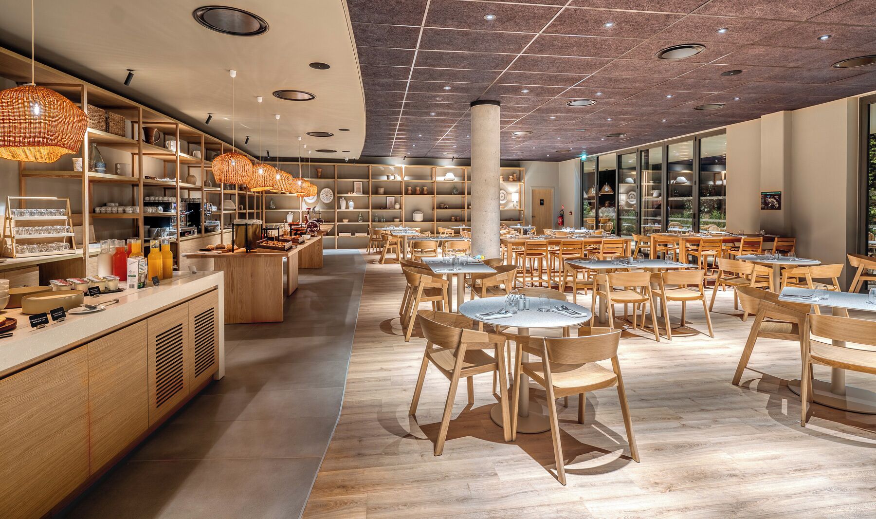 Un restaurante moderno con mobiliario de madera, una zona central de servicio e iluminación empotrada en el techo.