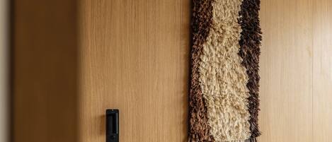 Habitación de hotel con cabecera de madera, un tapiz grande en la pared, una mesita de noche con control remoto y una cama con ropa blanca y dos almohadas.