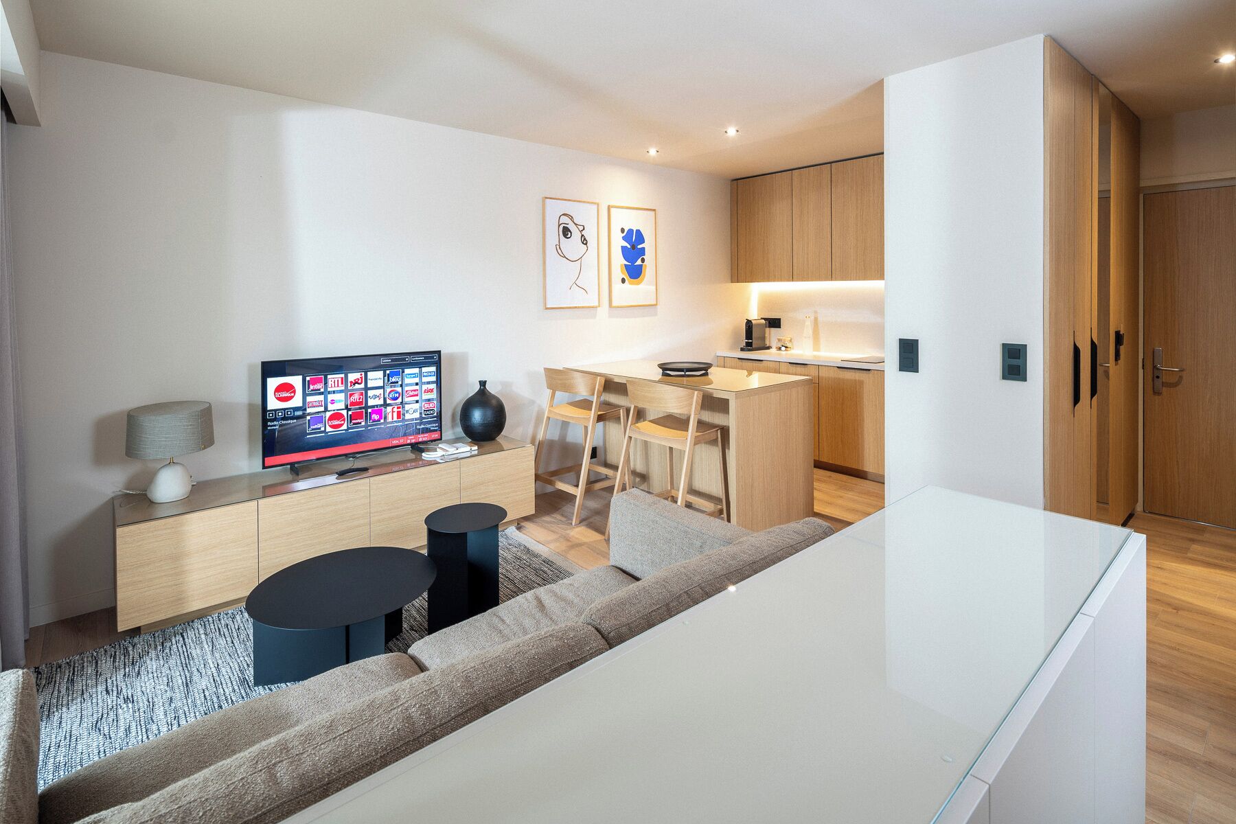 En moderne stue med et fladskærms-tv, en sofa, et sofabord og et spiseområde med et køkken i baggrunden.