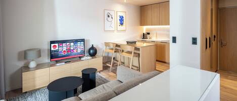 Un salon moderne doté d’un téléviseur à écran plat, d’un canapé, d’une table basse et d’un coin repas avec une cuisine en arrière-plan.