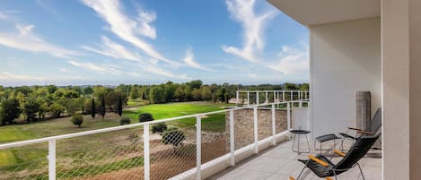 Varanda com vista para um campo de golfe, corrimão branco e duas cadeiras de balanço.