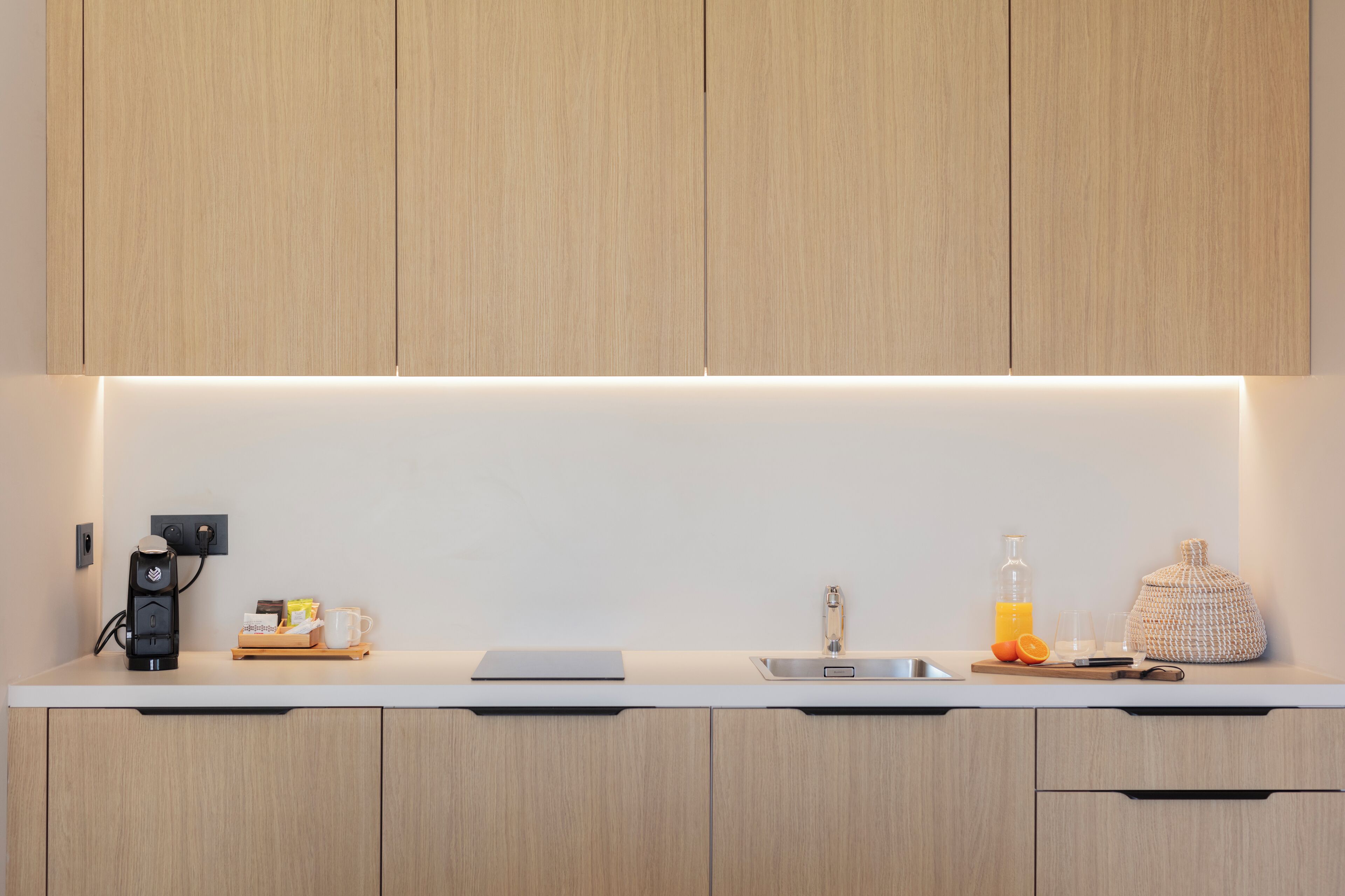 Een moderne keuken met houten kastjes, een inbouwspoelbak en een aanrecht met een koffiezetapparaat, een glas sinaasappelsap en een geweven bak.