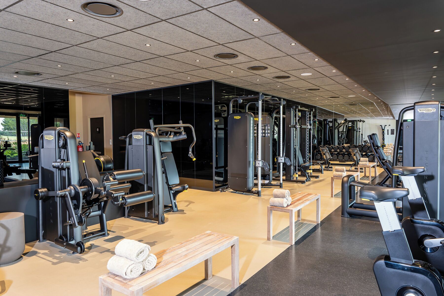 Un gimnasio con diversas máquinas de ejercicio, bancos y vistas al exterior.
