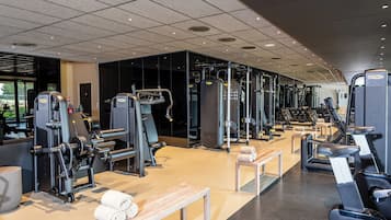 Un gimnasio con diversas máquinas de ejercicio, bancos y vistas al exterior.