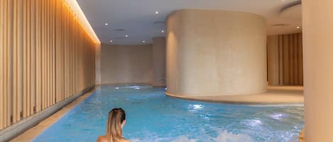 A large indoor swimming pool with a person in the water, surrounded by wooden paneling and a curved wall.