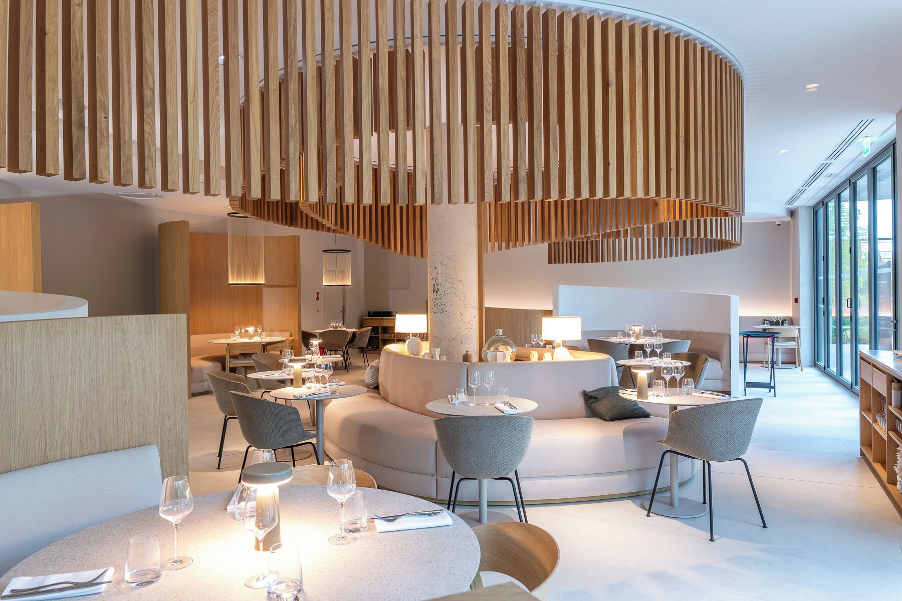 Un restaurante moderno con mesas redondas, sillas grises y una columna de madera central.