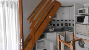 Eine kompakte Küche mit weißen Schränken, einer Mikrowelle, einer Kaffeemaschine und einer Waschmaschine.