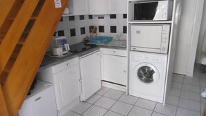 Eine kleine Küche mit weißen Schränken, einer Mikrowelle, einer Waschmaschine und einer Kaffeemaschine.