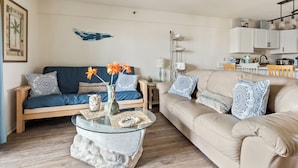A living room with a beige sofa, a blue sofa, and a glass coffee table with decorative items. - Studio with prime location next to Beach, Jolly Rogers and Boardwalk (Ocean City)